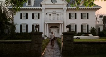 Movie still from “Jumanji” (1995), directed by Joe Johnston – A person walking down a path in front of a large white house; Wide shot, Low angle