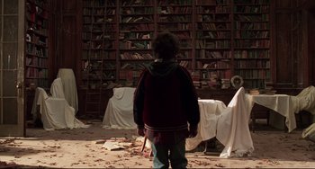 Movie still from “Jumanji” (1995), directed by Joe Johnston – A person standing in front of a book shelf; Wide shot, Low angle