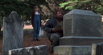 Movie still from “Jumanji” (1995), directed by Joe Johnston – A man and a woman standing in front of a grave marker; Wide shot, Over the shoulder angle