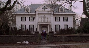 Movie still from “Jumanji” (1995), directed by Joe Johnston – Two people walking up the steps to a large white house; Extreme Wide shot, Low angle