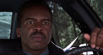 Movie still from “Jumanji” (1995), directed by Joe Johnston – A person in a car with trees in the background; Close Up shot, Low angle