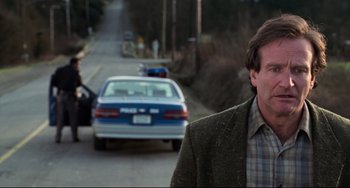 Movie still from “Jumanji” (1995), directed by Joe Johnston – A man standing on the side of a road next to a police car; Close Up shot, Over the shoulder angle