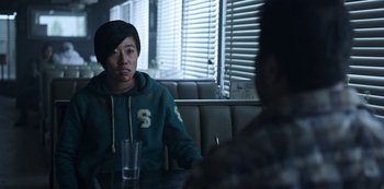 Movie still from “Black Summer” (2019), created by John Hyams – A person sitting at a table with a glass; Medium shot, Over the shoulder angle