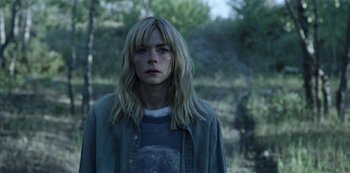 Movie still from “Black Summer” (2019), created by John Hyams – A woman with long blonde hair standing in the woods; Close Up shot, Low angle