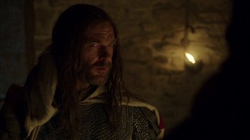 Movie still from “Knightfall” (2017), created by Richard Rayner – A man with long black hair wearing a chain mail outfit; Close Up shot, Over the shoulder angle