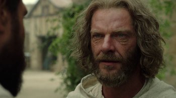 Movie still from “Knightfall” (2017), created by Richard Rayner – A person with long hair and a beard; Close Up shot, Over the shoulder angle