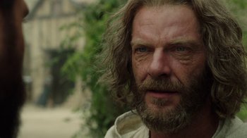 Movie still from “Knightfall” (2017), created by Richard Rayner – A person with long hair and a beard; Close Up shot, Over the shoulder angle