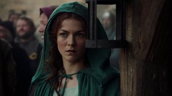 Movie still from “Knightfall” (2017), created by Richard Rayner – A woman in a green hooded robe standing in front of a window; Close Up shot, Over the shoulder angle