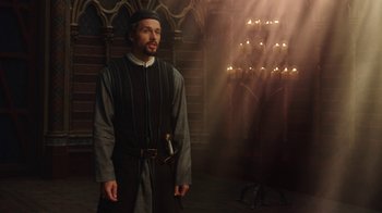 Movie still from “Knightfall” (2017), created by Richard Rayner – A man standing in front of a wall with candles; Medium shot, Over the shoulder angle
