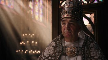 Movie still from “Knightfall” (2017), created by Richard Rayner – An older man wearing a crown in front of a stained glass window; Close Up shot, Low angle