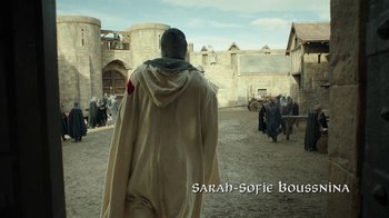 Movie still from “Knightfall” (2017), created by Richard Rayner – A man in a hooded jacket walking through a courtyard; Wide shot, High angle