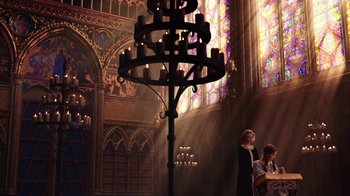 Movie still from “Knightfall” (2017), created by Richard Rayner – A candle stand in a church with people standing around it; Wide shot, Low angle