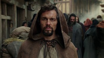 Movie still from “Knightfall” (2017), created by Richard Rayner – A man with a beard wearing a brown robe; Close Up shot, Low angle