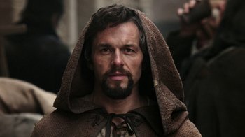 Movie still from “Knightfall” (2017), created by Richard Rayner – A man with a beard wearing a brown robe; Close Up shot, Low angle