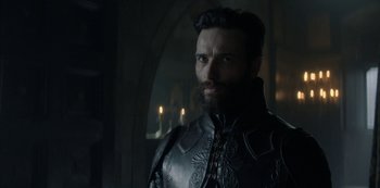 Movie still from “Knightfall” (2017), created by Richard Rayner – A man with a beard wearing a black armor; Close Up shot, Over the shoulder angle