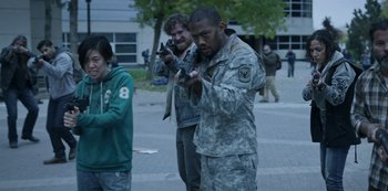 Movie still from “Black Summer” (2019), created by John Hyams – A group of people standing on a sidewalk holding toy guns; Medium shot, Over the shoulder angle