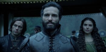 Movie still from “Knightfall” (2017), created by Richard Rayner – A man with a beard wearing a leather suit; Close Up shot, Over the shoulder angle