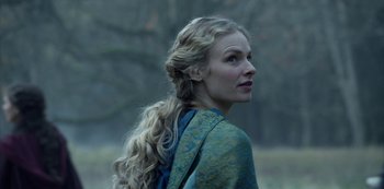 Movie still from “Knightfall” (2017), created by Richard Rayner – A woman with long blonde hair wearing a blue and green dress; Close Up shot, Over the shoulder angle