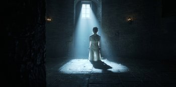 Movie still from “Knightfall” (2017), created by Richard Rayner – A woman in a white dress standing in the light of a window; Wide shot, Low angle