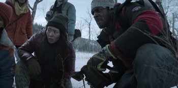 Movie still from “Black Summer” (2019), created by John Hyams – A group of people standing in the snow near a tree; Medium shot, Low angle