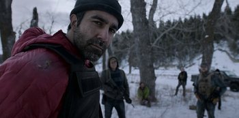 Movie still from “Black Summer” (2019), created by John Hyams – A group of people standing in the snow near a tree; Medium shot, Over the shoulder angle