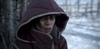 Movie still from “Black Summer” (2019), created by John Hyams – A young woman wearing a hooded jacket in the snow; Close Up shot, Over the shoulder angle