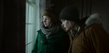 Movie still from “Black Summer” (2019), created by John Hyams – Two people standing next to each other in front of a window; Medium shot, Low angle