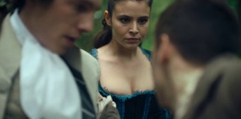 Movie still from “La Révolution” (2020), directed by Jérémie Rozan – A woman in a blue dress standing next to two men; Close Up shot, Over the shoulder angle