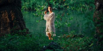 Movie still from “La Révolution” (2020), directed by Jérémie Rozan – A woman in a white dress standing next to a body of water; Wide shot, High angle