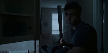 Movie still from “Black Summer” (2019), created by John Hyams – A man holding a baseball bat while standing in a room; Medium shot, Low angle