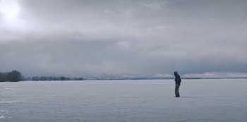 Movie still from “Black Summer” (2019), created by John Hyams – A man standing in the snow with a snowboard; Extreme Wide shot, Low angle