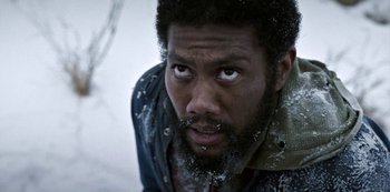 Movie still from “Black Summer” (2019), created by John Hyams – A person with a beard looking at the camera; Close Up shot, Low angle