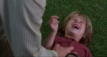 Movie still from “Liar Liar” (1997), directed by Tom Shadyac – A young child laughing while laying on the grass; Close Up shot, Over the shoulder angle