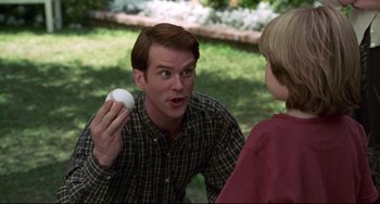 Movie still from “Liar Liar” (1997), directed by Tom Shadyac – A man holding an object up to his mouth; Medium shot, Over the shoulder angle