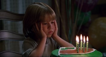 Movie still from “Liar Liar” (1997), directed by Tom Shadyac – A young boy sitting in front of a birthday cake with lit candles; Close Up shot, High angle