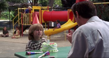 Movie still from “Liar Liar” (1997), directed by Tom Shadyac – A little boy wearing a party hat sitting in front of a birthday cake; Medium shot, Over the shoulder angle
