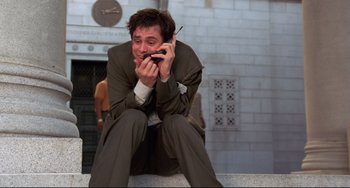 Movie still from “Liar Liar” (1997), directed by Tom Shadyac – A man sitting on the ground talking on a cell phone; Medium shot, Low angle