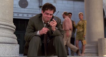 Movie still from “Liar Liar” (1997), directed by Tom Shadyac – A man sitting on the ground holding a cell phone; Medium shot, Low angle