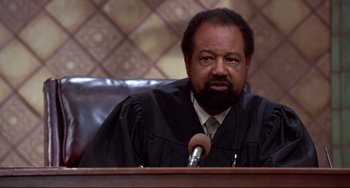 Movie still from “Liar Liar” (1997), directed by Tom Shadyac – A man wearing a black robe and holding a microphone in his hand; Close Up shot, High angle