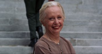 Movie still from “Liar Liar” (1997), directed by Tom Shadyac – An older woman smiling for the camera with her hands behind her back; Close Up shot, Low angle