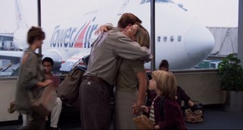 Movie still from “Liar Liar” (1997), directed by Tom Shadyac – A man and a woman hug at an airport while a young girl watches; Medium shot, Over the shoulder angle