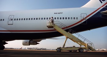 Movie still from “Liar Liar” (1997), directed by Tom Shadyac – A man standing on the stairs of an airplane; Wide shot, Low angle