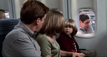 Movie still from “Liar Liar” (1997), directed by Tom Shadyac – A little boy sitting next to two adults on an airplane; Medium shot, Over the shoulder angle