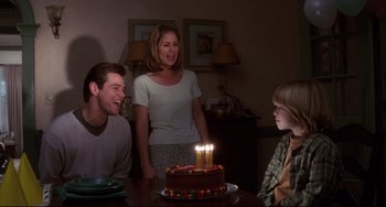 Movie still from “Liar Liar” (1997), directed by Tom Shadyac – A woman and two men sitting at a table with a cake with candles on it; Medium shot, Over the shoulder angle