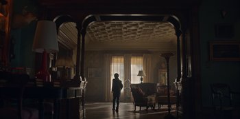 Movie still from “Locke & Key” (2020), created by Carlton Cuse – A person standing in a living room looking out a window; Wide shot, Low angle