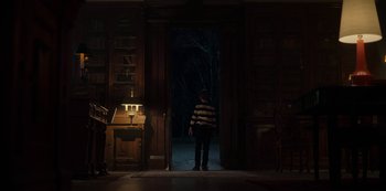 Movie still from “Locke & Key” (2020), created by Carlton Cuse – A man standing in front of an open door in a dark room; Wide shot, Low angle