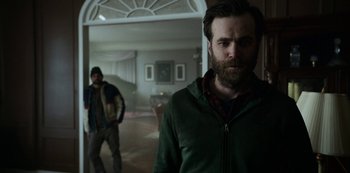 Movie still from “Black Summer” (2019), created by John Hyams – A man with a beard standing next to another man in a room; Medium shot, Over the shoulder angle