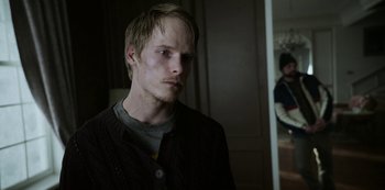 Movie still from “Black Summer” (2019), created by John Hyams – A young man standing in front of a mirror in a room; Close Up shot, Over the shoulder angle