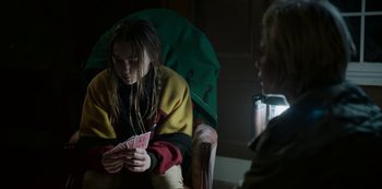 Movie still from “Black Summer” (2019), created by John Hyams – A woman sitting in a chair playing cards with another woman; Medium shot, Over the shoulder angle