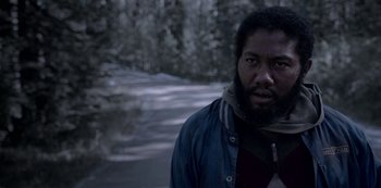 Movie still from “Black Summer” (2019), created by John Hyams – A man standing on a road in the middle of a forest; Close Up shot, Low angle